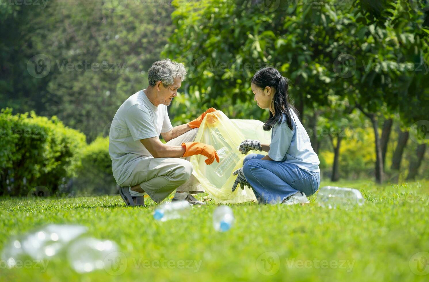 grandfather support granddaughter to collect plastic garbage,sorting plastic bottles waste in the park,concept of raising awareness of volunteerism,environmental conservation,ecology photo