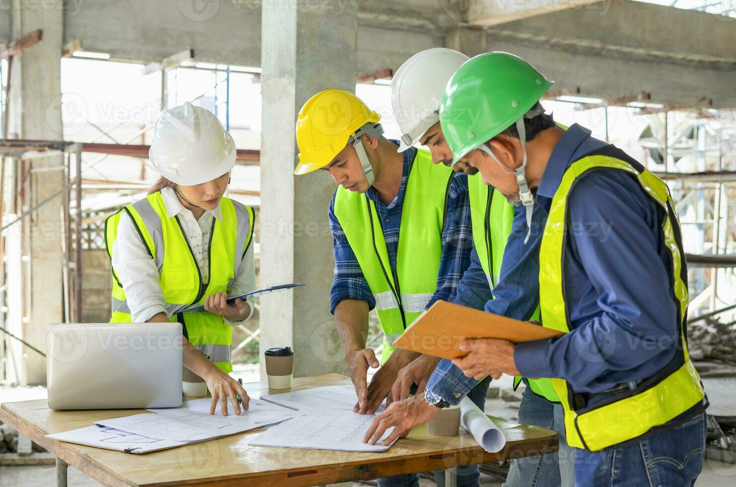 engineering teamwork wearing full safety gear discussing with blueprint and laptop on table in a new building under construction,engineers project manager consultation meeting with coworker photo