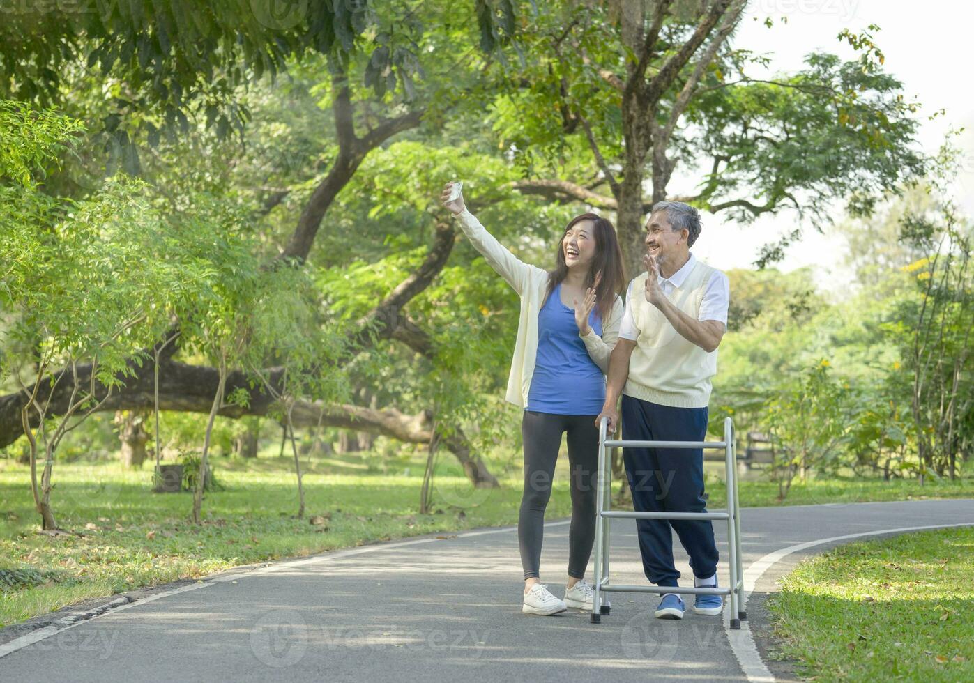 father and daughter enjoy walking in the park, senior man walking with walker, the daughter doing selfie and laughing together. family relationship concept photo
