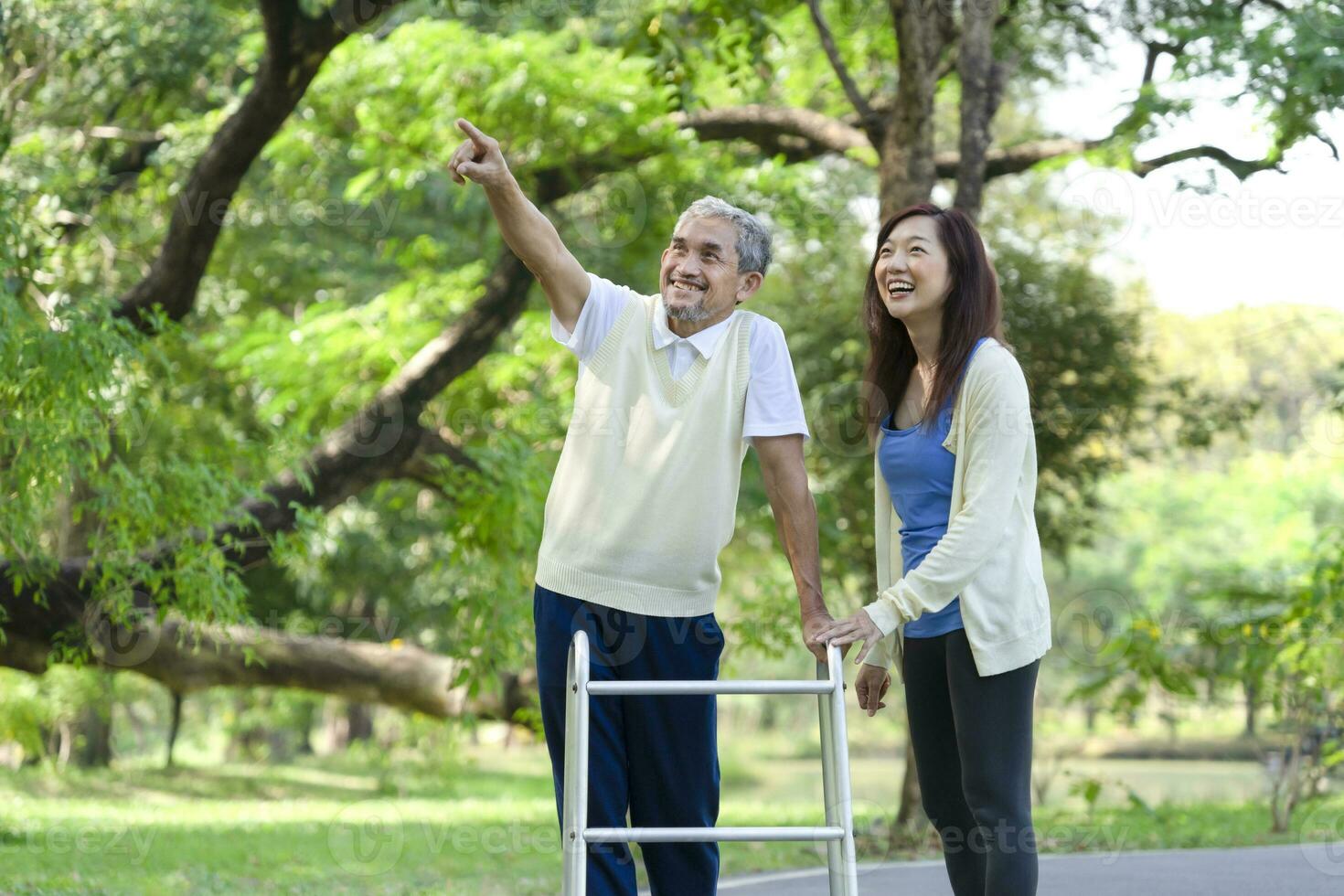 father and daughter enjoy walking in the park, senior man walking with walker, the father pointing index to something and laughing together. family relationship concept photo