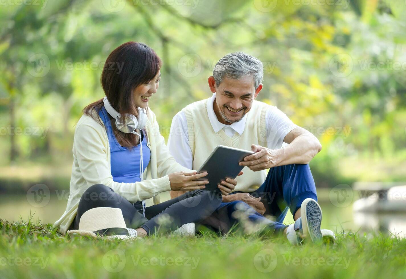 smiling father and daughter enjoy looking at tablet online together while relaxing in park on springtime,concept for elderly people lifestyle, relaxing,wellbeing,family relationship, love of a family photo