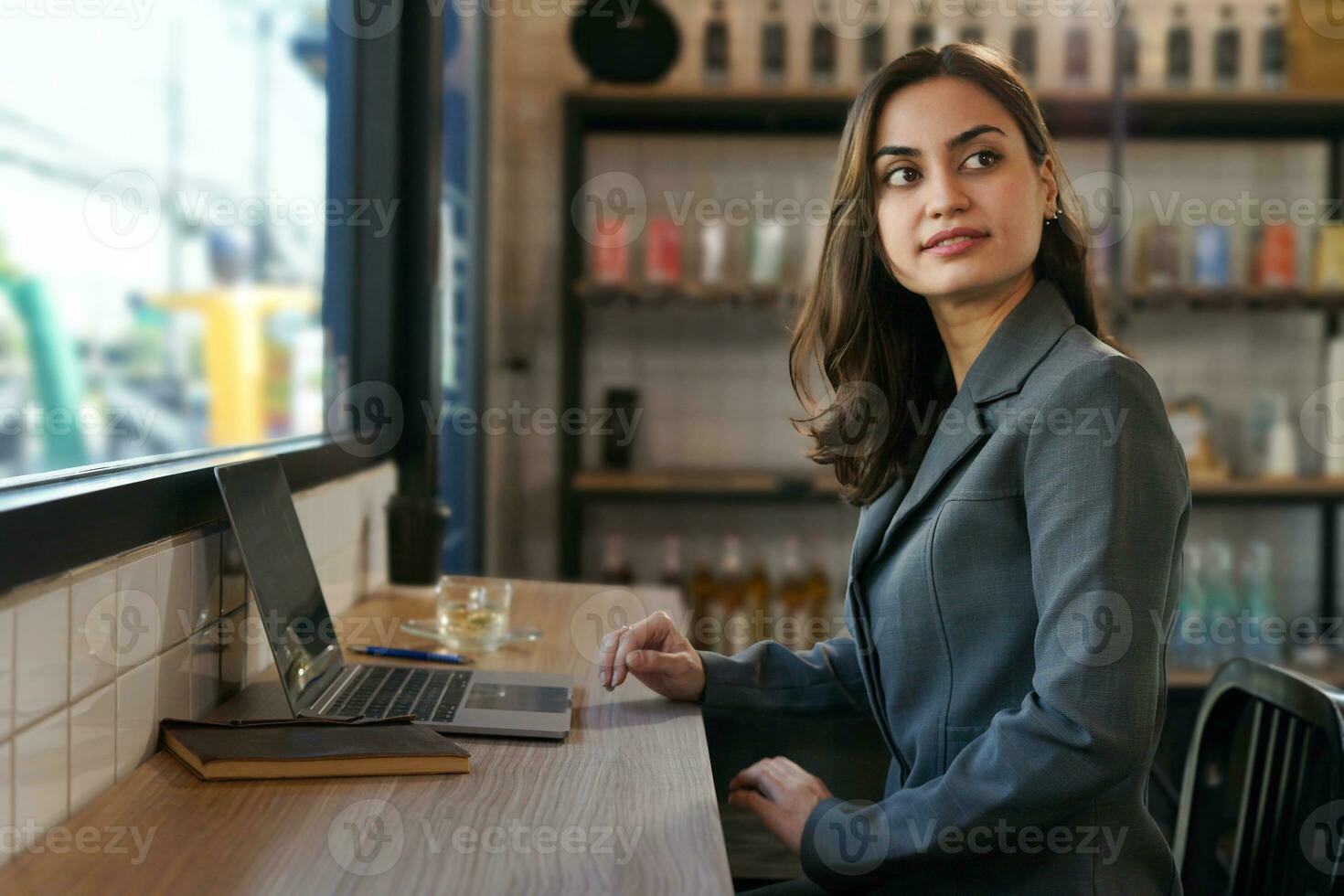 attractive business woman in suit sitting at counter bar, young modern female remote work, a digital nomad working over laptop internet online in cafe indoors photo
