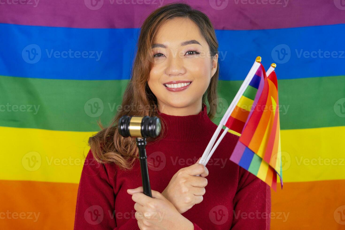 happy young asian woman smile, one hand holding lgbtq rainbow flag and other hand holding judge hammer, support of lgbtq community equality movement, respect gay pride, lgbt happy pride month photo