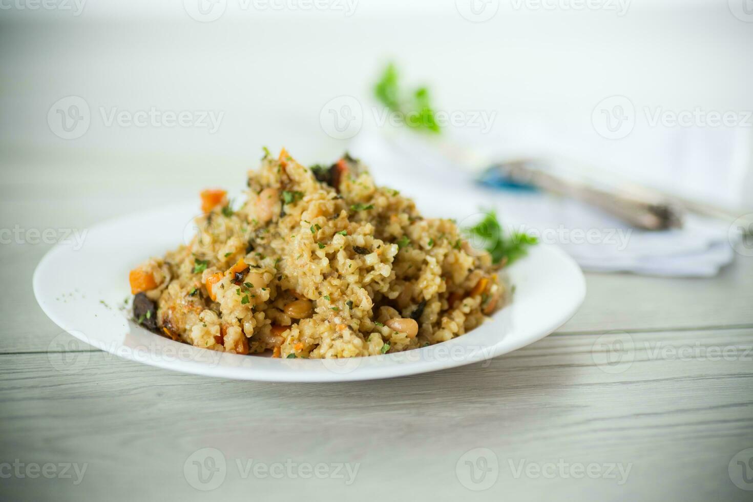 cooked bulgur with vegetables, carrots and dried mushrooms in a plate . photo