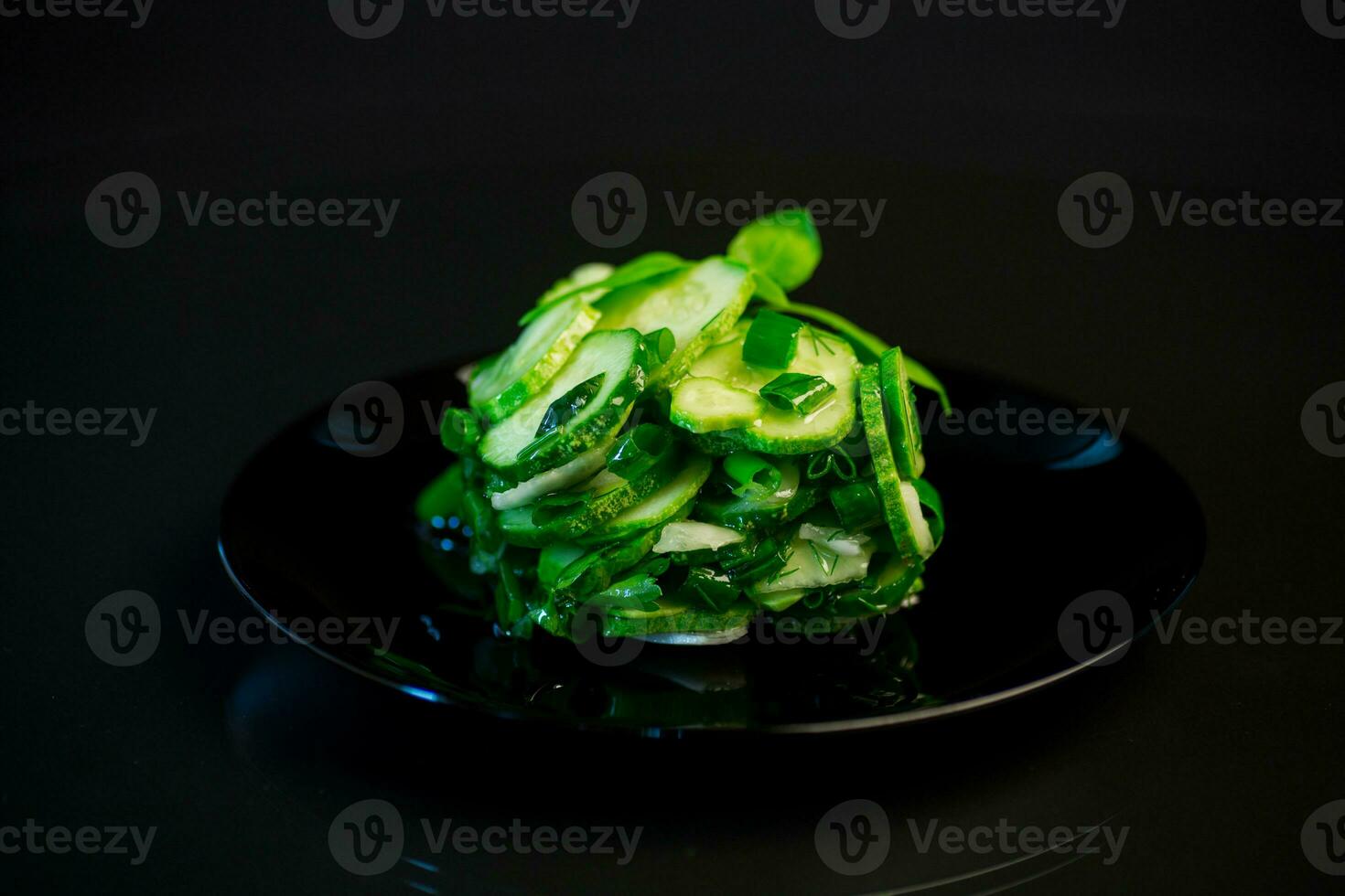 salad of fresh cucumbers with herbs and onions in a plate on a black background. photo