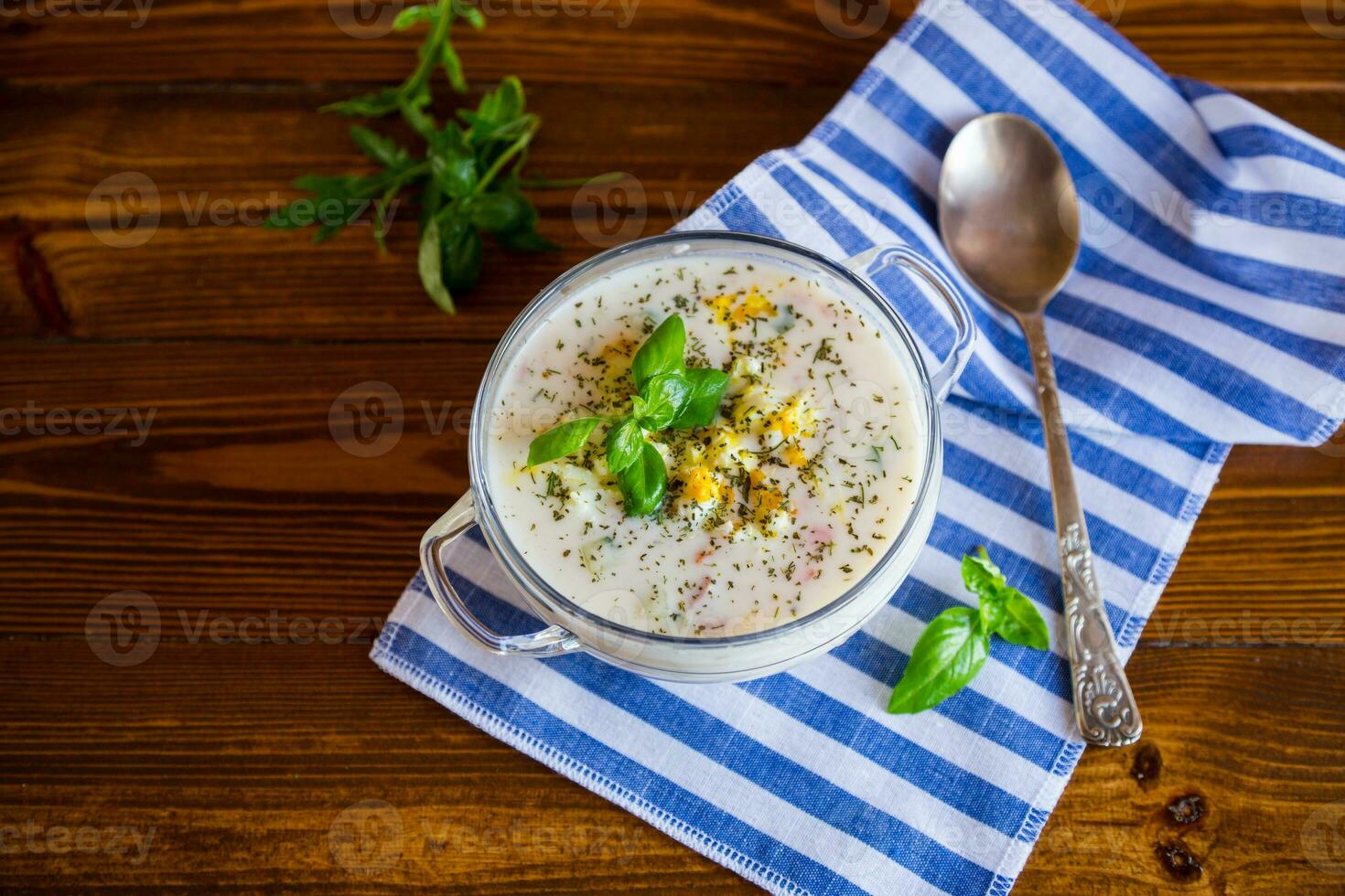Cold soup with cucumbers, eggs, vegetables, yogurt and fresh herbs in a glass bowl . photo