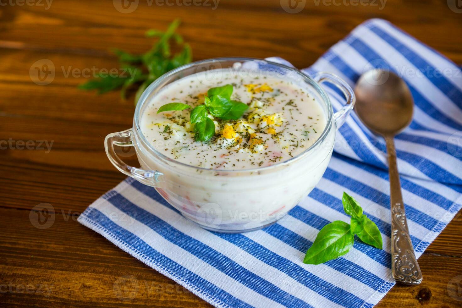 Cold soup with cucumbers, eggs, vegetables, yogurt and fresh herbs in a glass bowl . photo