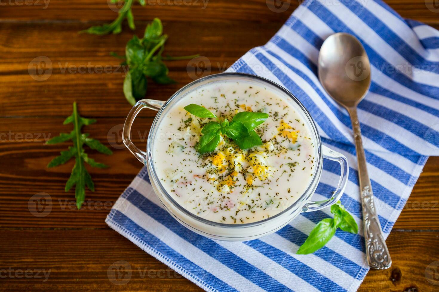 Cold soup with cucumbers, eggs, vegetables, yogurt and fresh herbs in a glass bowl . photo
