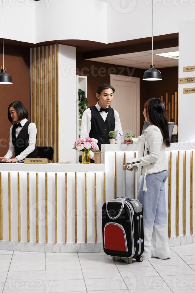 turista llega a elegante recurso y es preparando a hacer el cheque en a el recepción. hembra invitado es bienvenido por simpático y servicial personal a el frente escritorio de acogedor hotel. foto