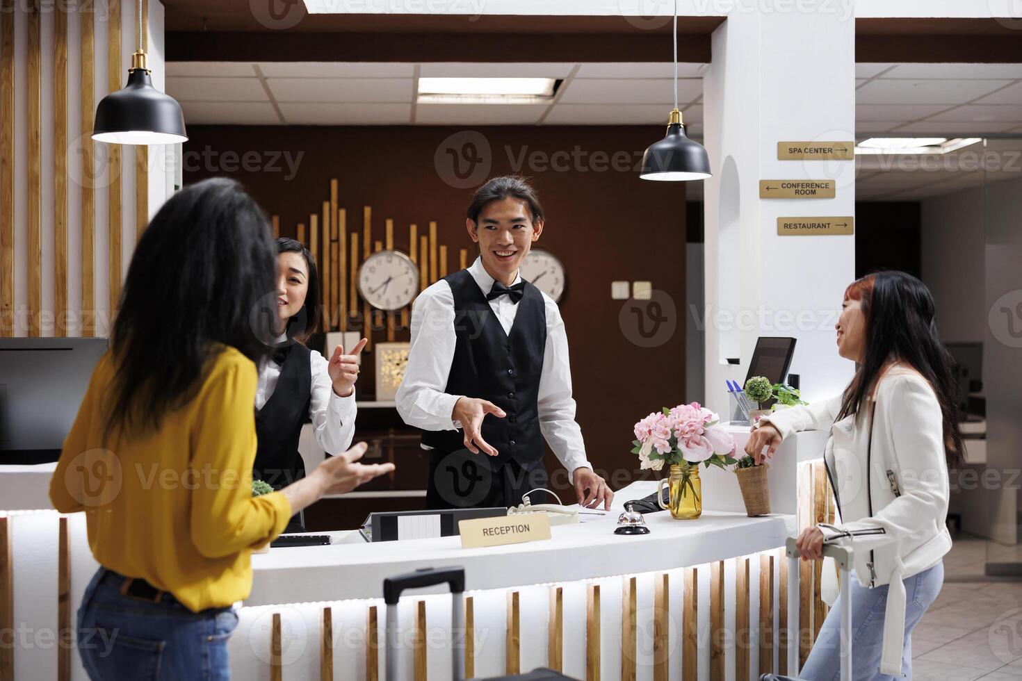 Young asian receptionist offering direction to arriving customer in lobby of luxuriant hotel. Smiling female concierge guiding traveler to accommodation at receptionist desk photo