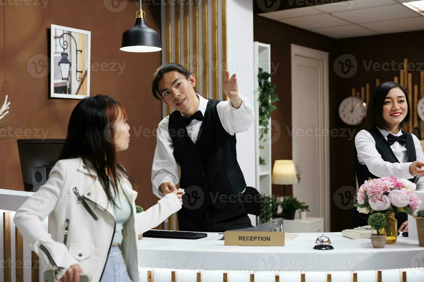 Woman being guided by helpful asian receptionist while on holiday in modern hotel lobby. Traveler starting trip in entrance of extravagant resort, receiving room card key photo