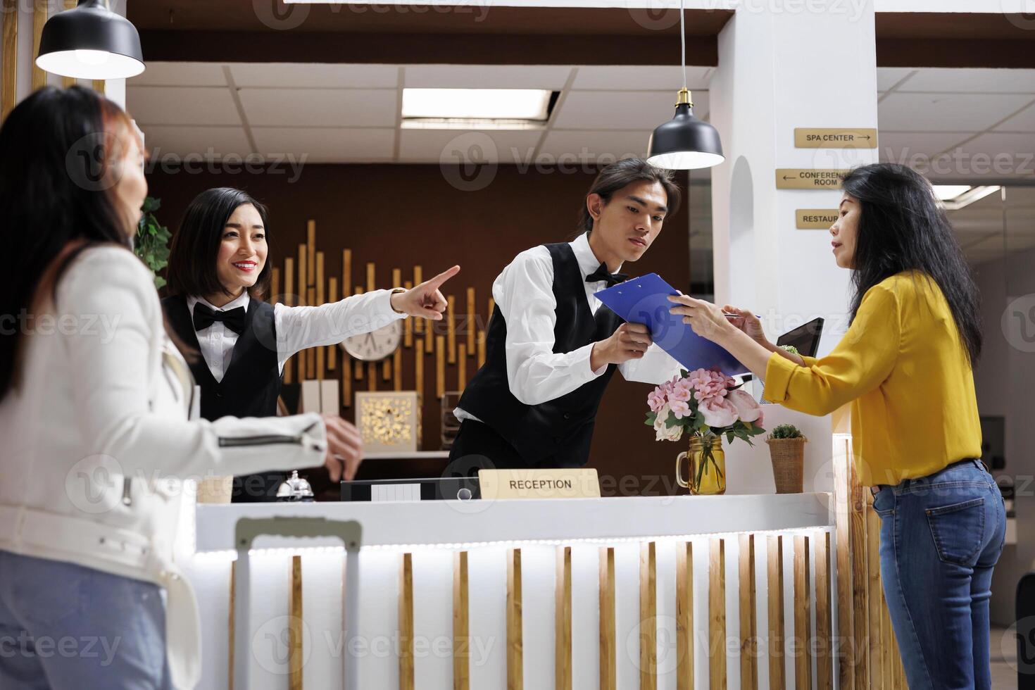 Hotel guest receives registration form from asian male receptionist to make room reservation. Smiling female concierge giving direction to customer at front desk of cozy resort photo
