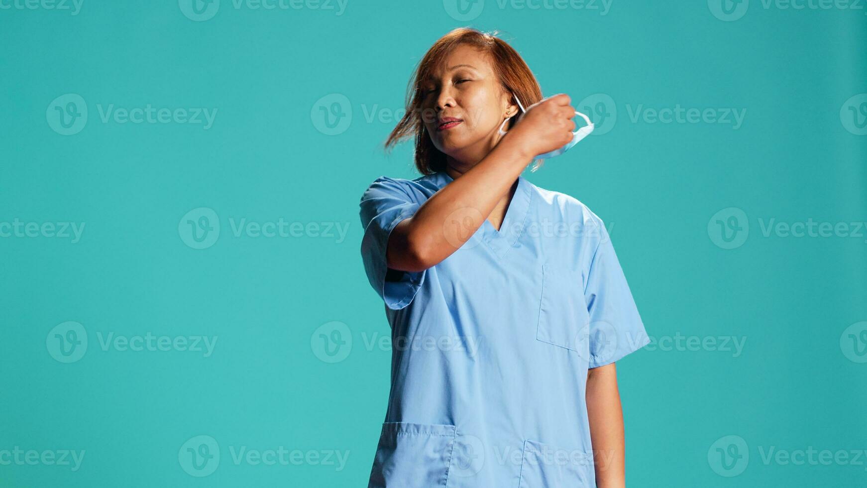 Exhausted nurse happy to take off antibacterial facemask after finishing job shift. Healthcare expert pleased to finally remove suffocating protective mask, isolated over studio background, close up photo