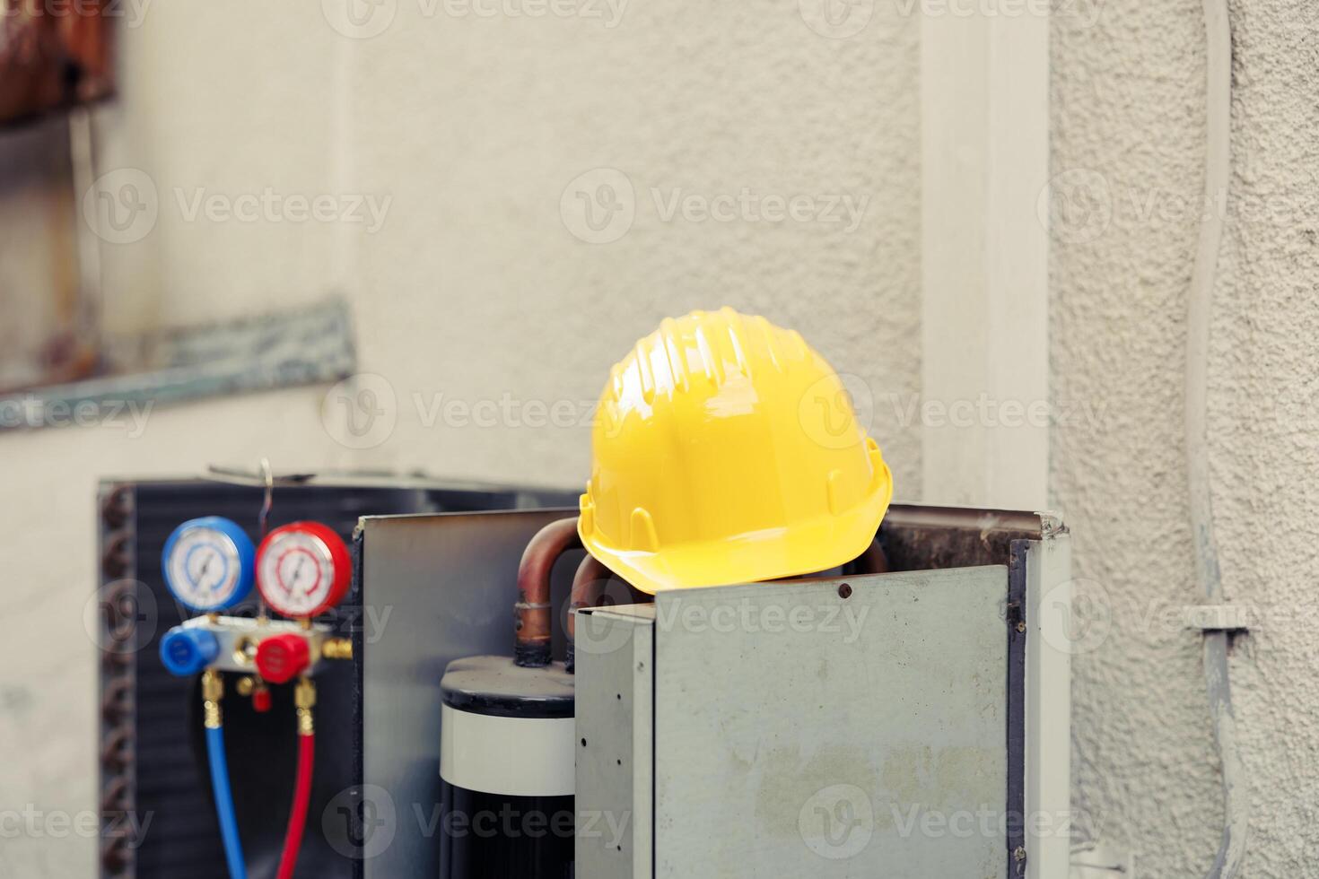 Close up of yellow protection helmet on top of out of service external air conditioner unit in need of repair. Outdoor opened HVAC system with manifold gauges and safety gear photo