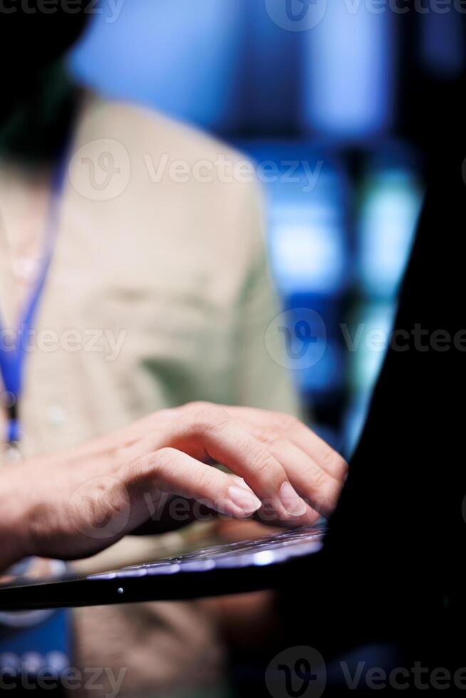 Close up shot of system admin doing maintenance, writing checklist on laptop of needed repairments in server farm housing advanced data storage equipment supporting critical IT workloads photo