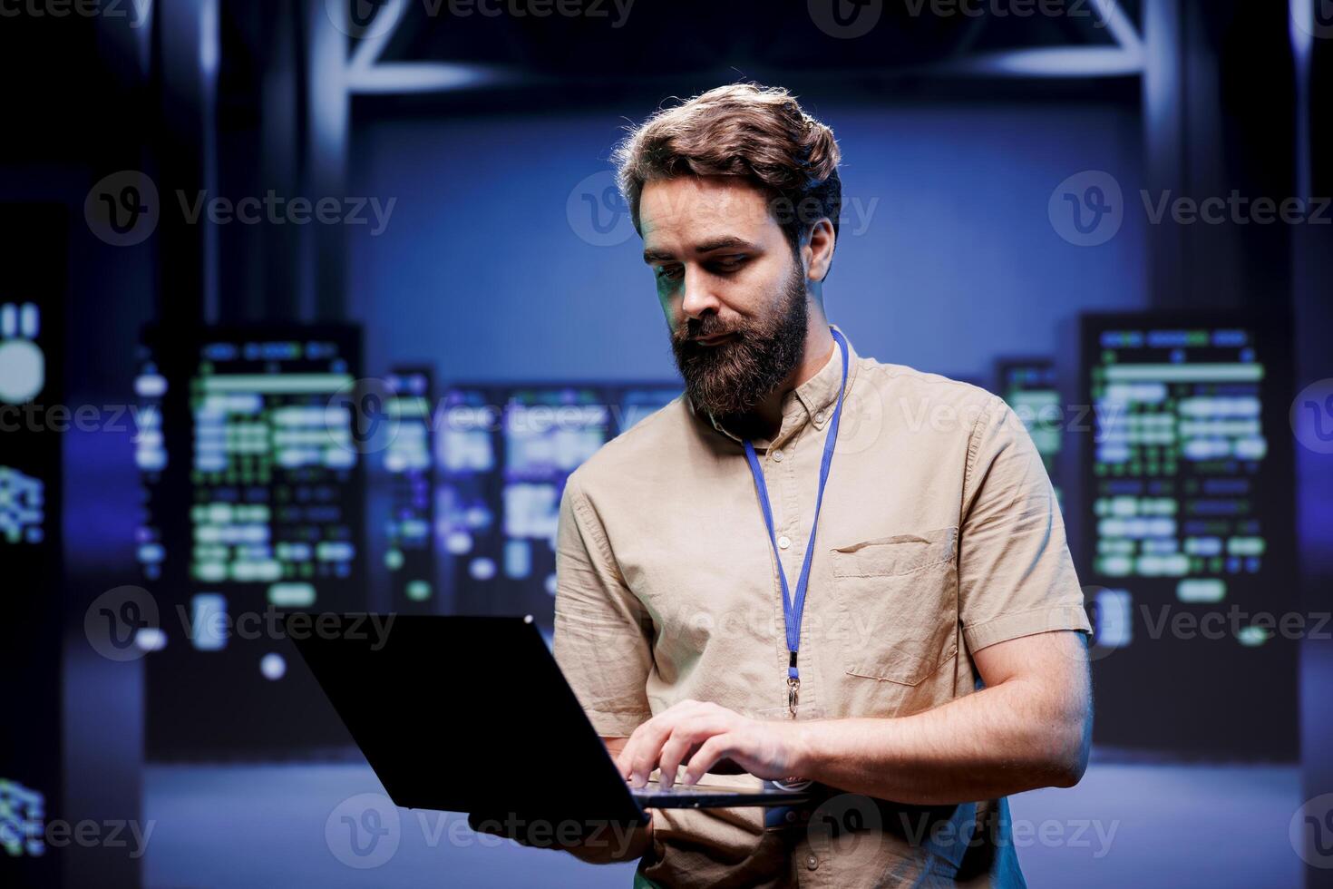 Computer programmer in high tech room housing mainframes, storage devices and networking systems providing large amounts of computing resources. Employee doing server cabinets maintenance using laptop photo