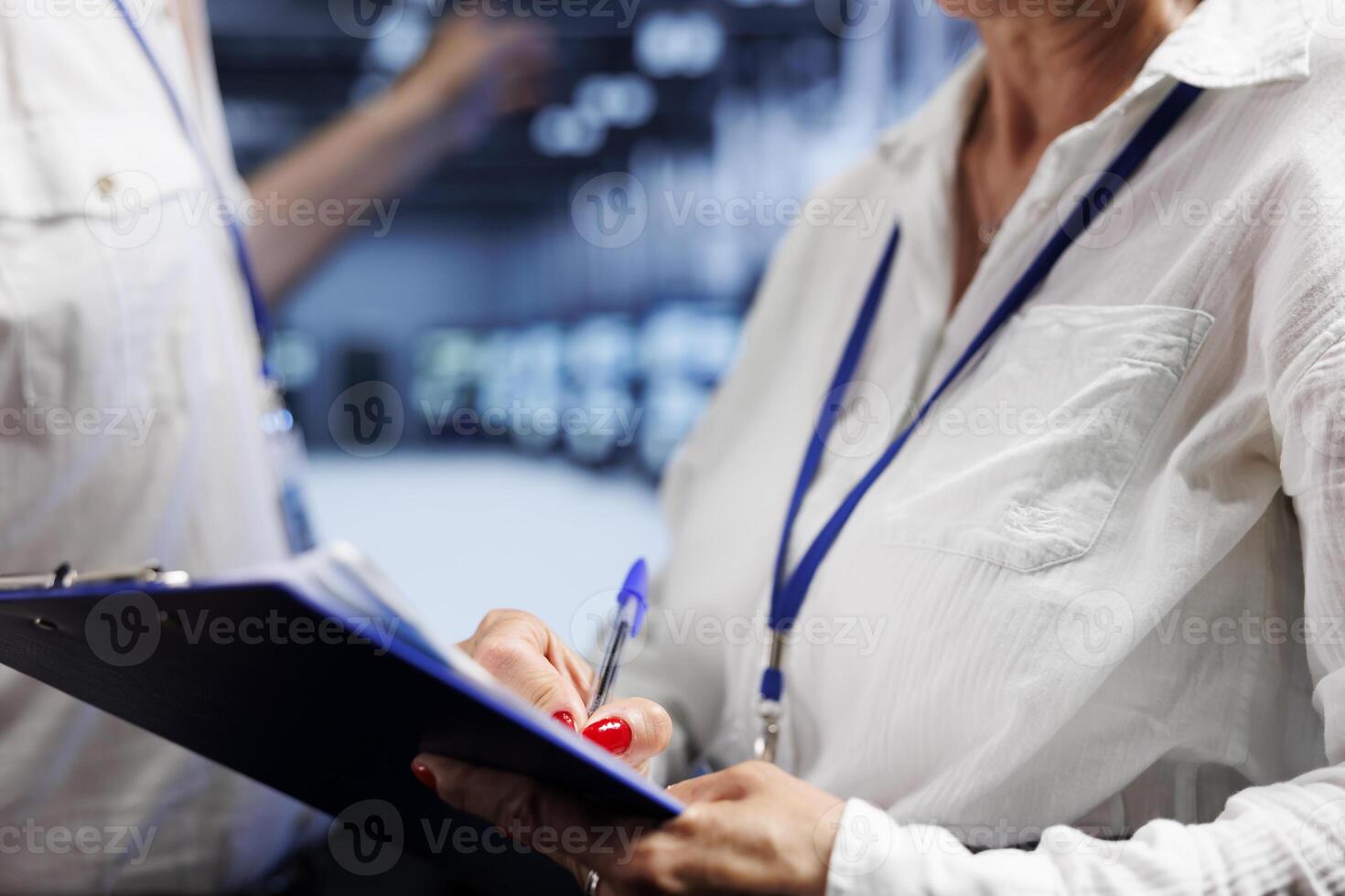 Technical support consultants performing diagnostic assessment on server cabinets to detect problems with data center units. Employees diligently reviewing maintenance list examining for system issues photo