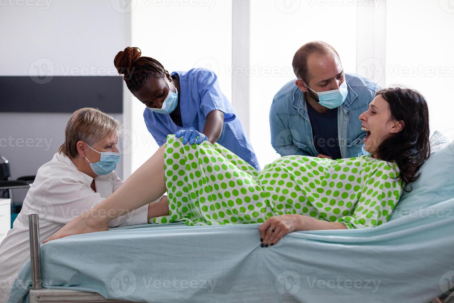 Pregnant woman lying in bed giving birth to baby in hospital ward while