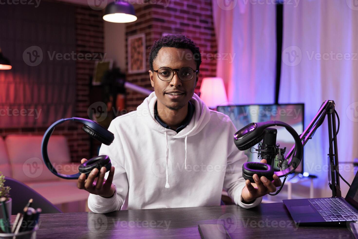 Portrait of technology vlogger comparing and reviewing over the ear headphones in living room studio. Knowledgeable content creator filming audiophiles channel vlog for streaming service photo