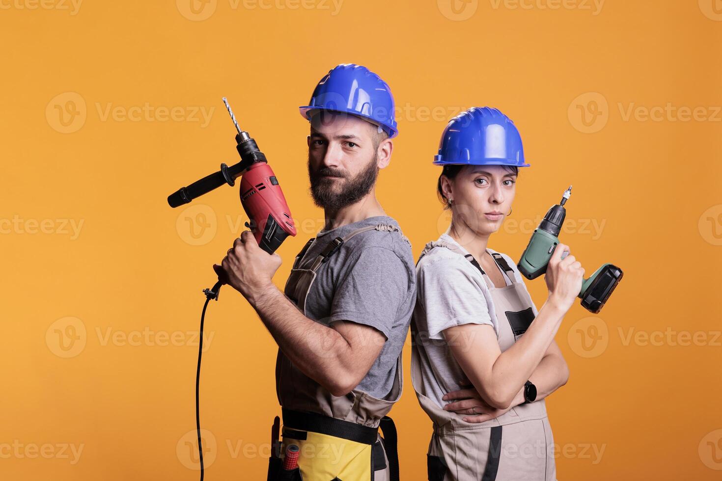 Confident renovators standing with electric power drills, looking at camera and acting confident in studio. Team of builders holding drilling gun tools to work on renovation, refurbishment. photo
