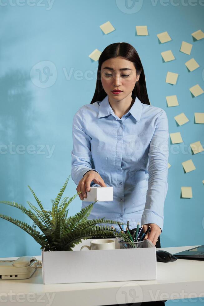 Female project analyst taking home personal items after being fired from the corporate workplace. Disgruntled asian office worker collecting belongings after getting dismissed for job performance. photo