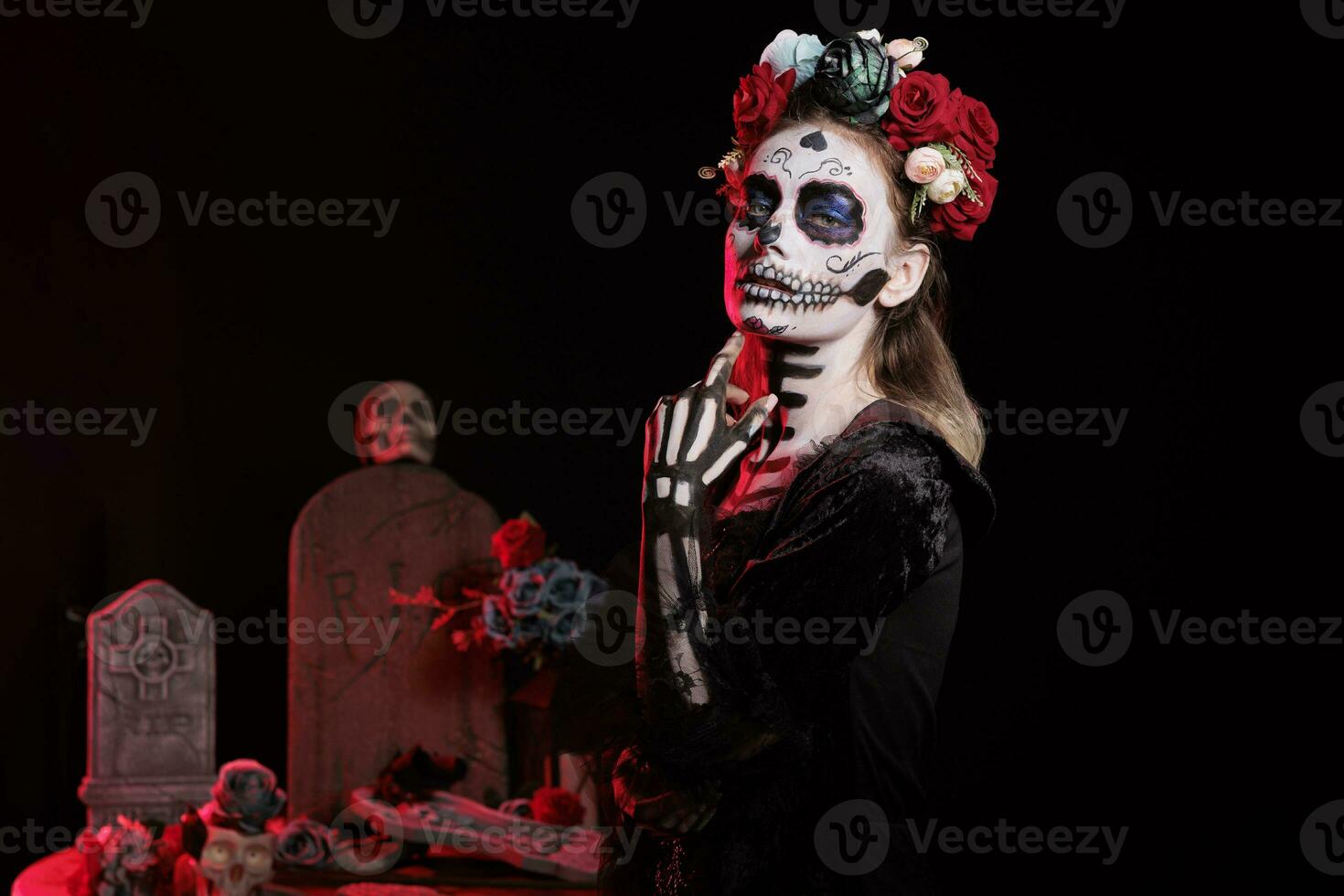 Horror lady of death wearing black glamorous costume in studio, looking like holy santa muerte with flowers crown. Acting creepy and posing dressed as goddess of dead on dios de los muertos. photo