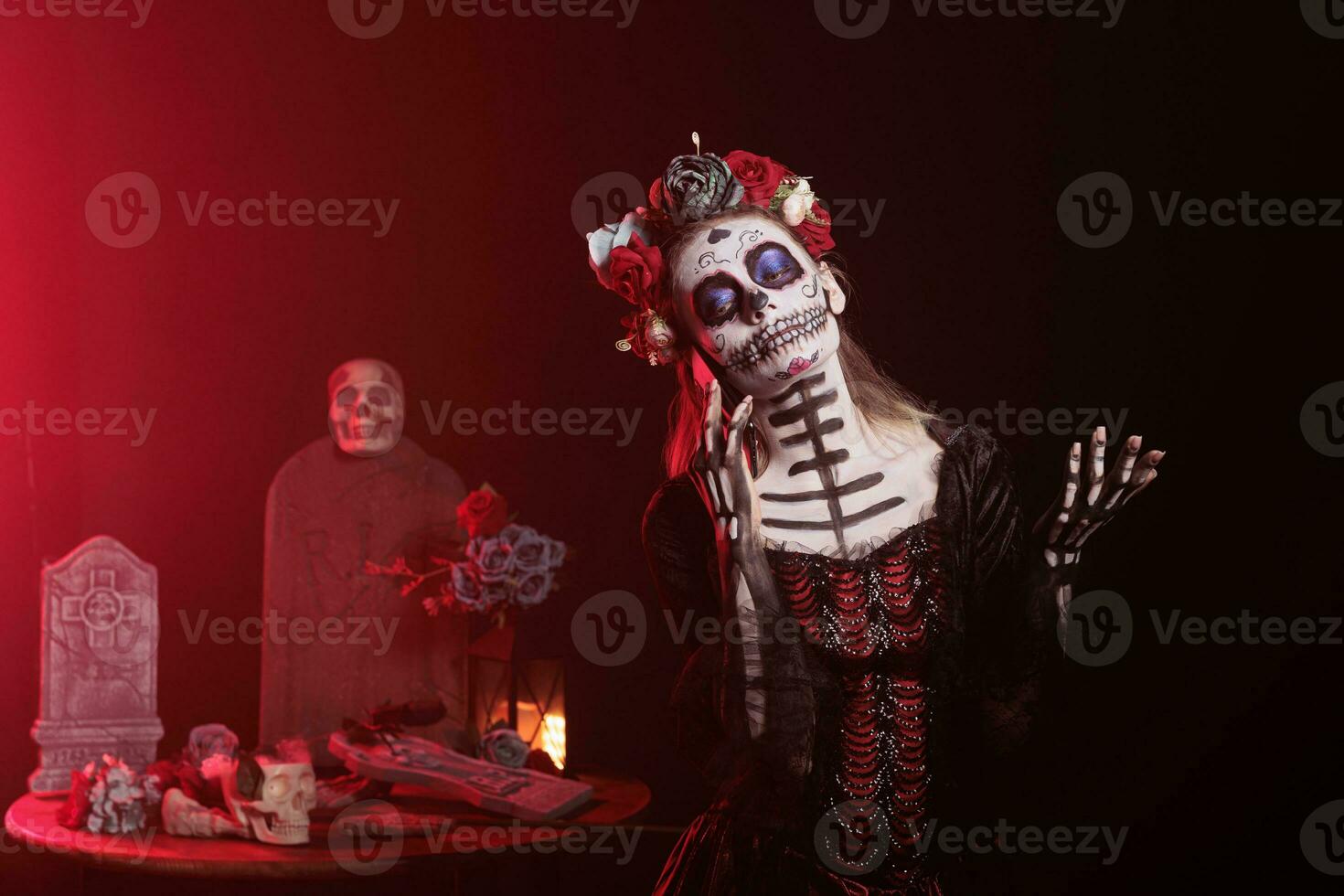 Scary woman talking on mobile phone call, wearing halloween make up and flowers crown in studio. La cavalera catrina using smartphone line on dios de los muertos mexican tradition. photo