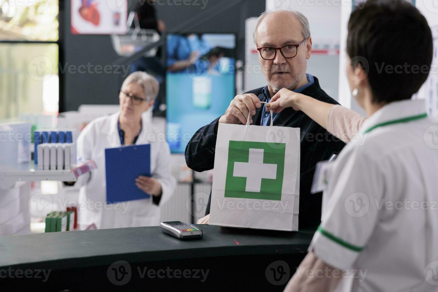 Medical store employee giving purchase package to senior man at cash register. Pharmaceutical assistant giving shopping paper bag to elderly customer at drugstore paydesk photo