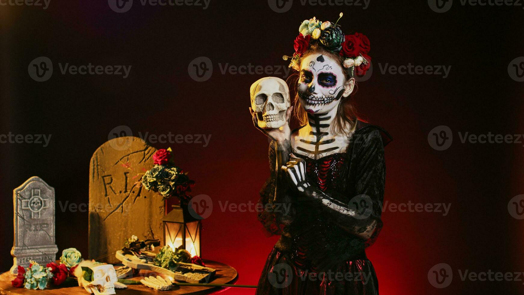 Creepy horror model posing with skull in studio, acting spooky on mexican halloween dios de los muertos. Flirty woman looking like la cavalera catrina to celebrate traditional culture. photo