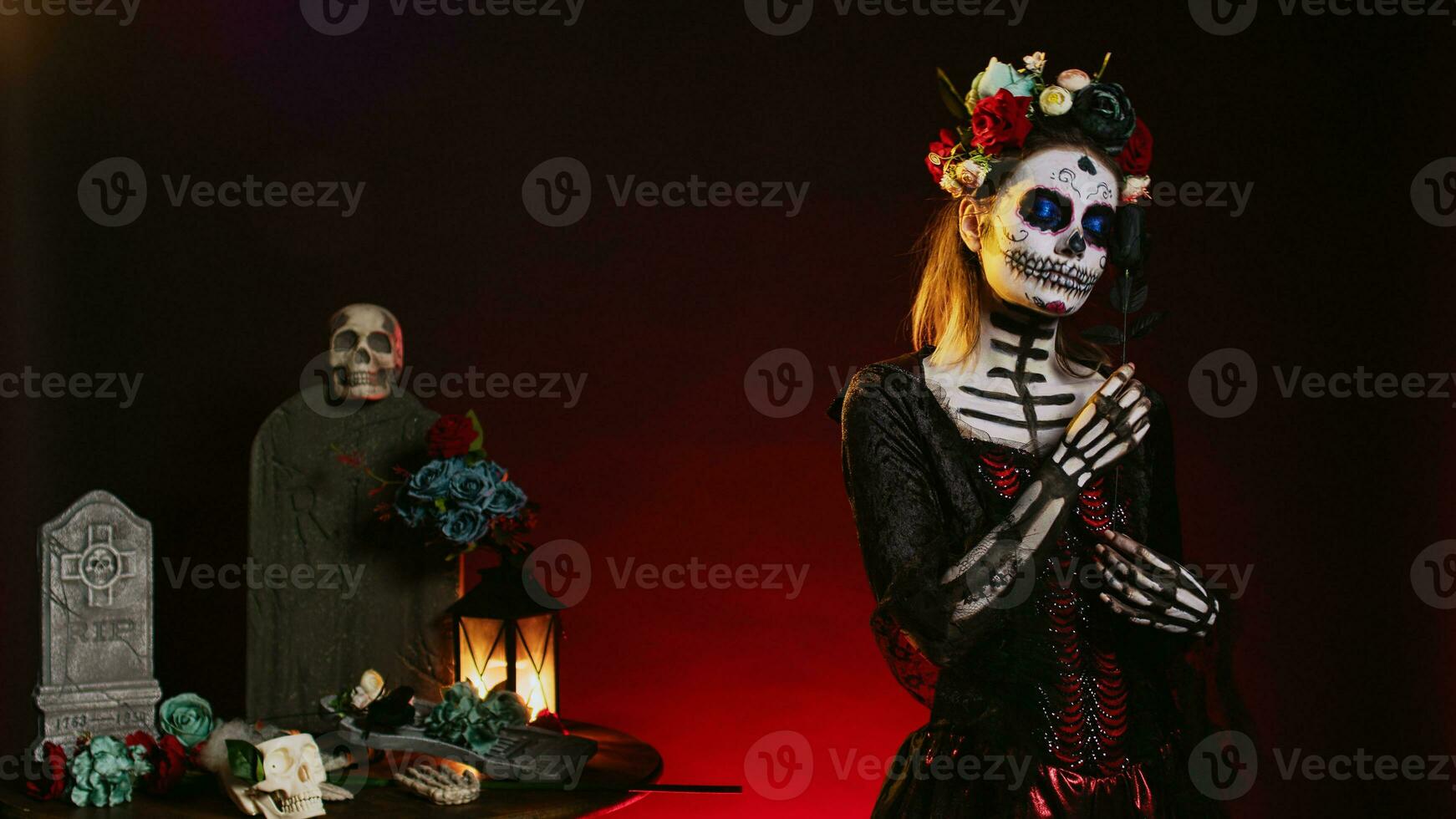 Flirty woman wearing santa muerte body art in studio, acting glamorous on day of the dead mexican halloween celebration. Ritual skull body art, posing with black roses and flowers crown. photo