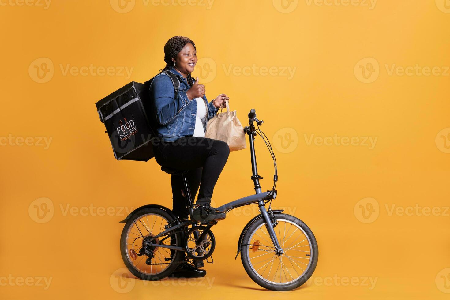 Pizzeria employee holding paper bag full with takeaway food order delivering to client during lunch time, courier doing thumbs up gesture at camera. Deliverywoman using bike as transportation photo