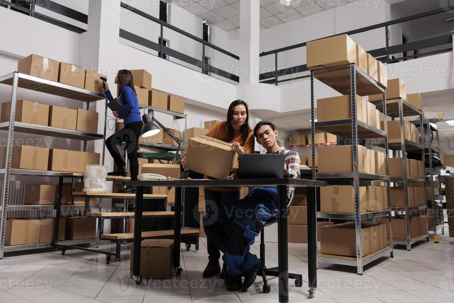 Postal service workers checking parcel invoice on laptop before dispatching while working in storage room. Storehouse employees analyzing freight customs clearance information on computer photo