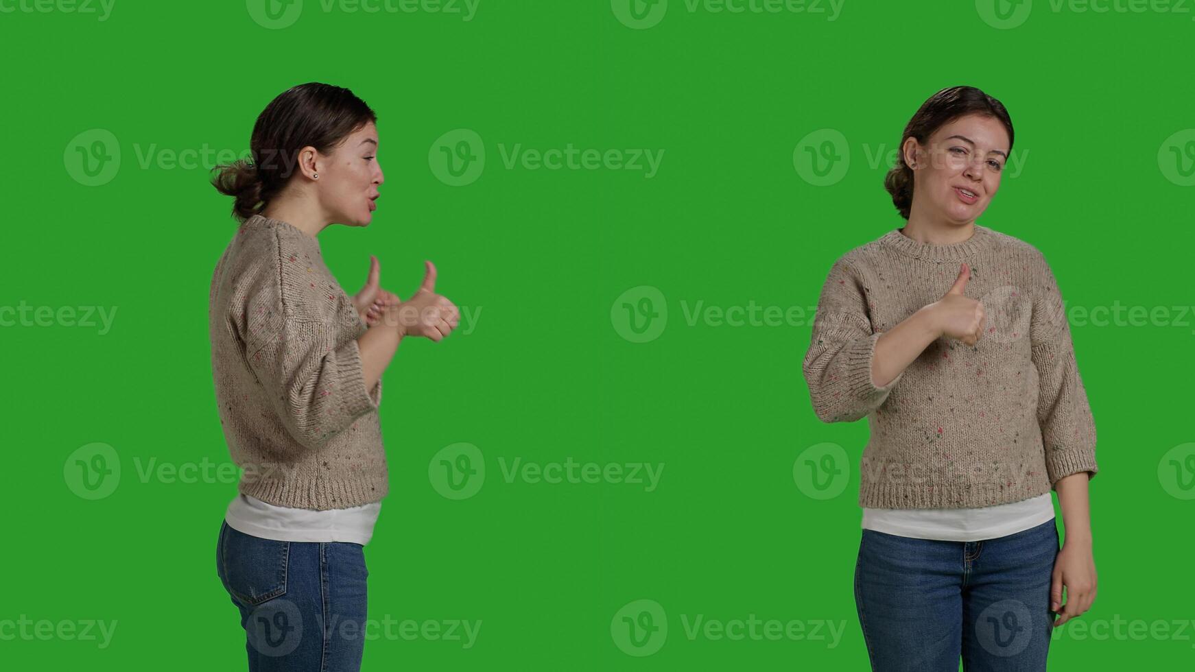 Cheerful model doing thumbs up symbol in studio, expressing approval and like gesture over greenscreen. Female person acting positive and happy, showing agreement and okay good sign. photo