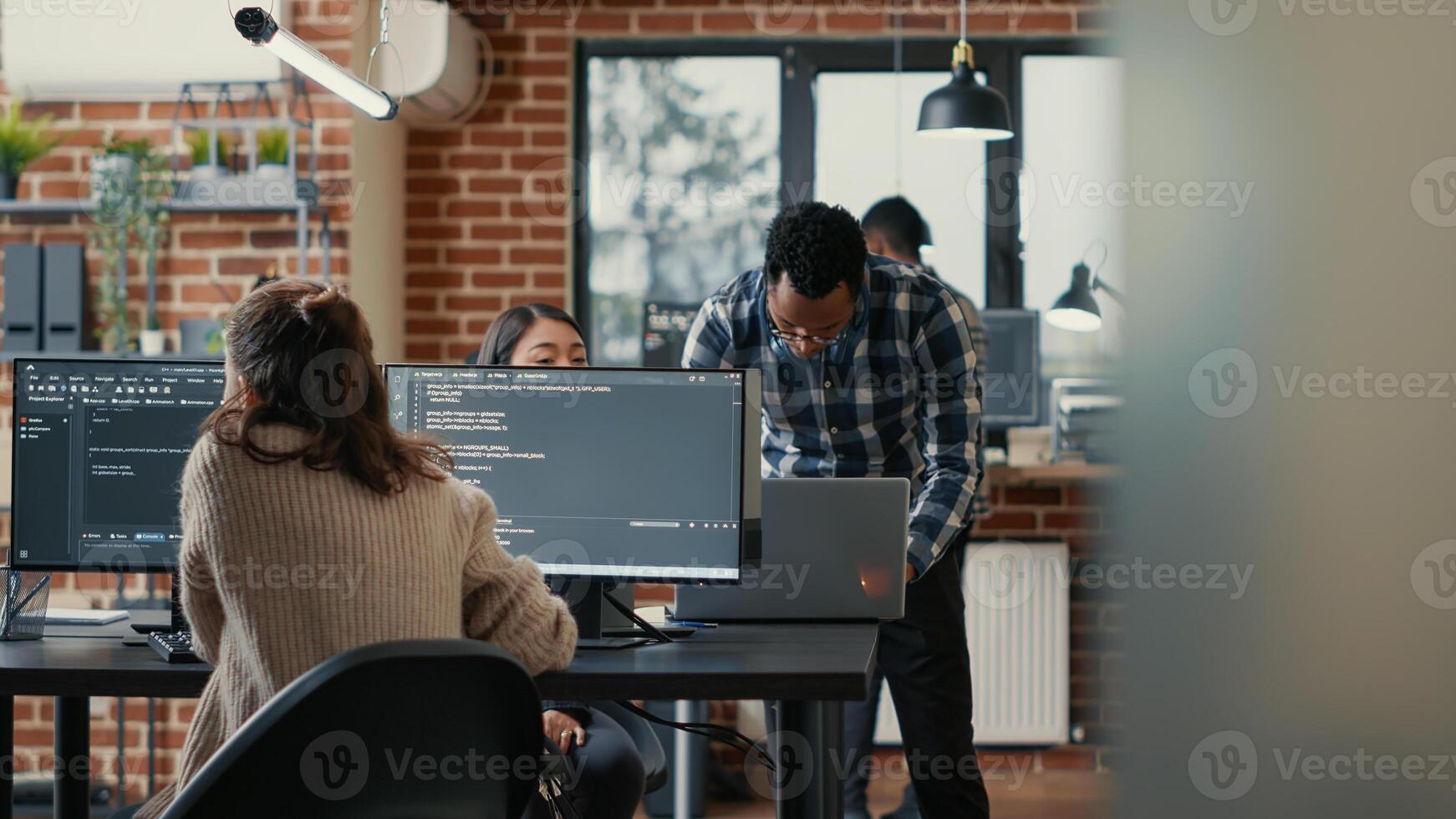 Database programer writing code in front of multiple computer screens displaying artificial intelligence algorithm. Developer coding database while colleagues doing teamwork in background. photo