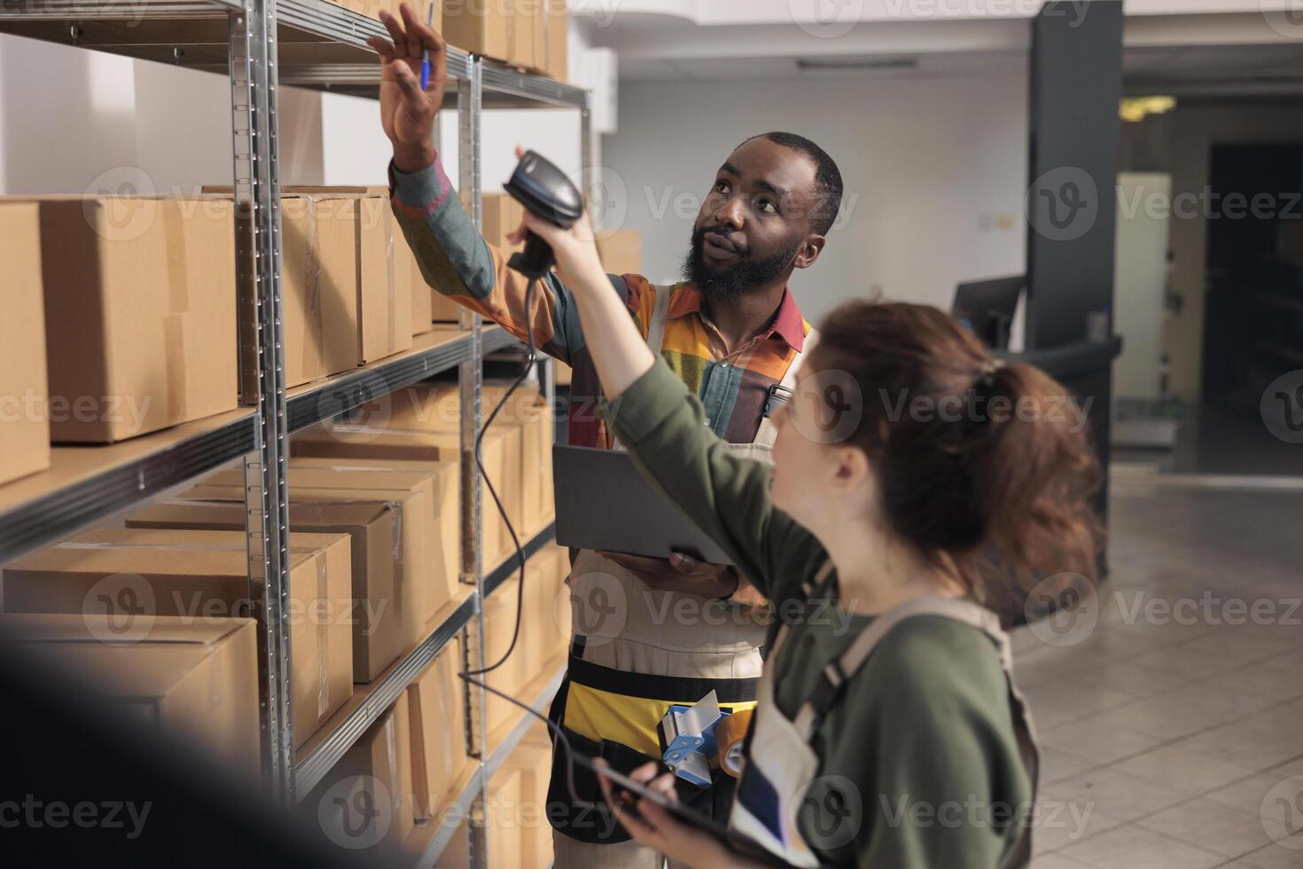 Storehouse supervisor showing colleague invoice code on device to find clients parcel in storage room. Shipping service employees scanning merchandise products while analyzing logistics report photo
