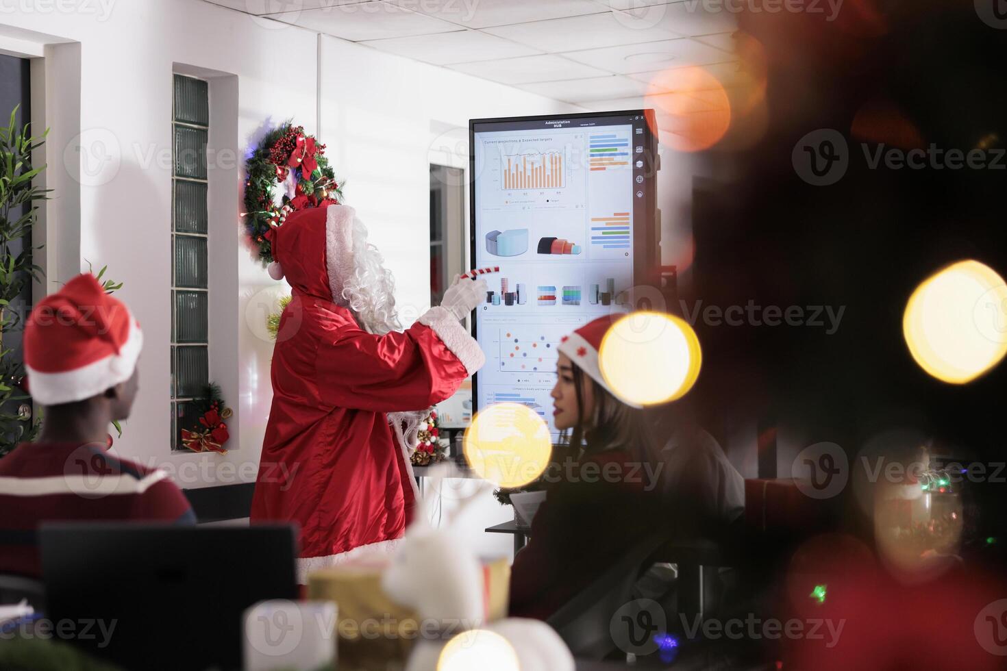 Industry leader dressed as Santa Claus teaching employees important lesson in Christmas ornate boardroom. Corporate orator showing business statistics visualization data to workers photo