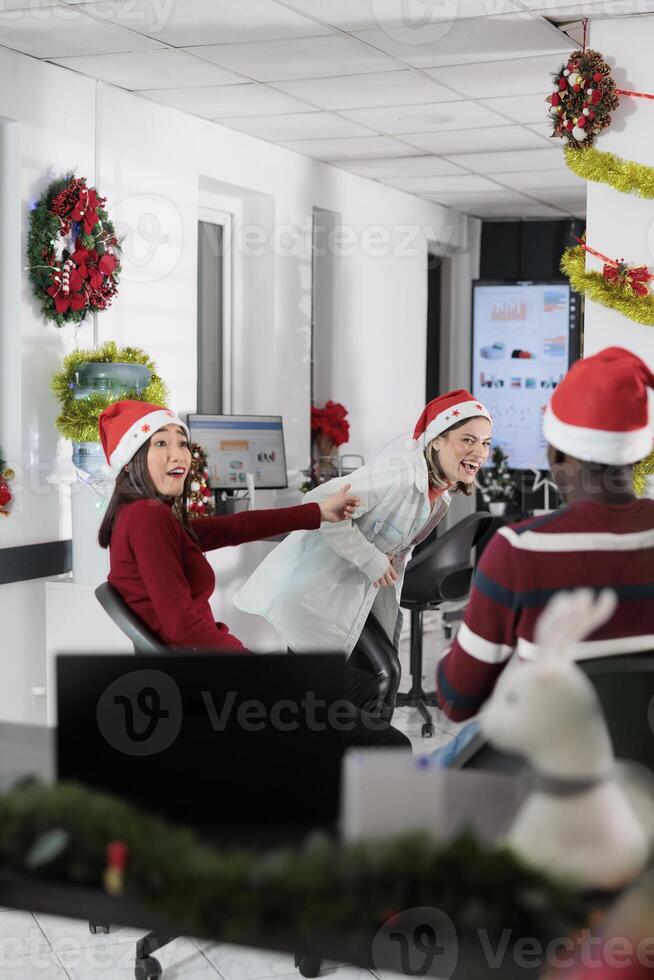 Colleagues having fun in xmas ornate office, making fun of each other at work during Christmas holiday season. Staff members laughing together in xmas adorn boardroom during coffee break photo
