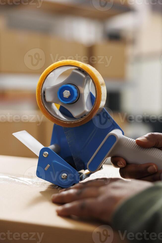 Warehouse employee preparing customers packages for delivery using adhesive tape, doing products quality control in storehouse. Stockroom manager working at online orders in storage room photo