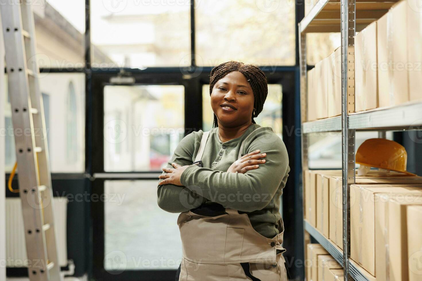 Warehouse worker standing with arm crossed smiling at camera while working at goods inventory. African american employee preparing customers order before strat delivery packages in storehouse photo