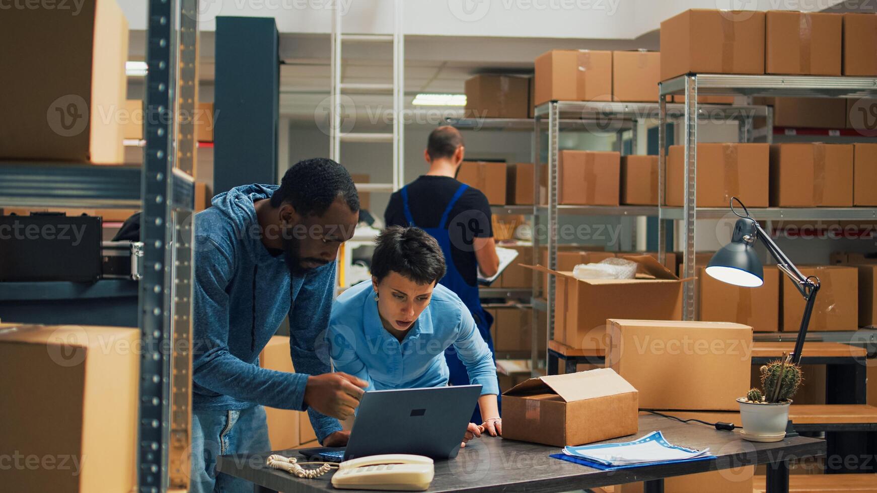 Offce employees doing teamwork to ship goods in cardboard boxes, checking quality of merchandise in storehouse space. Diverse owners using laptop to plan products shipment distribution. photo