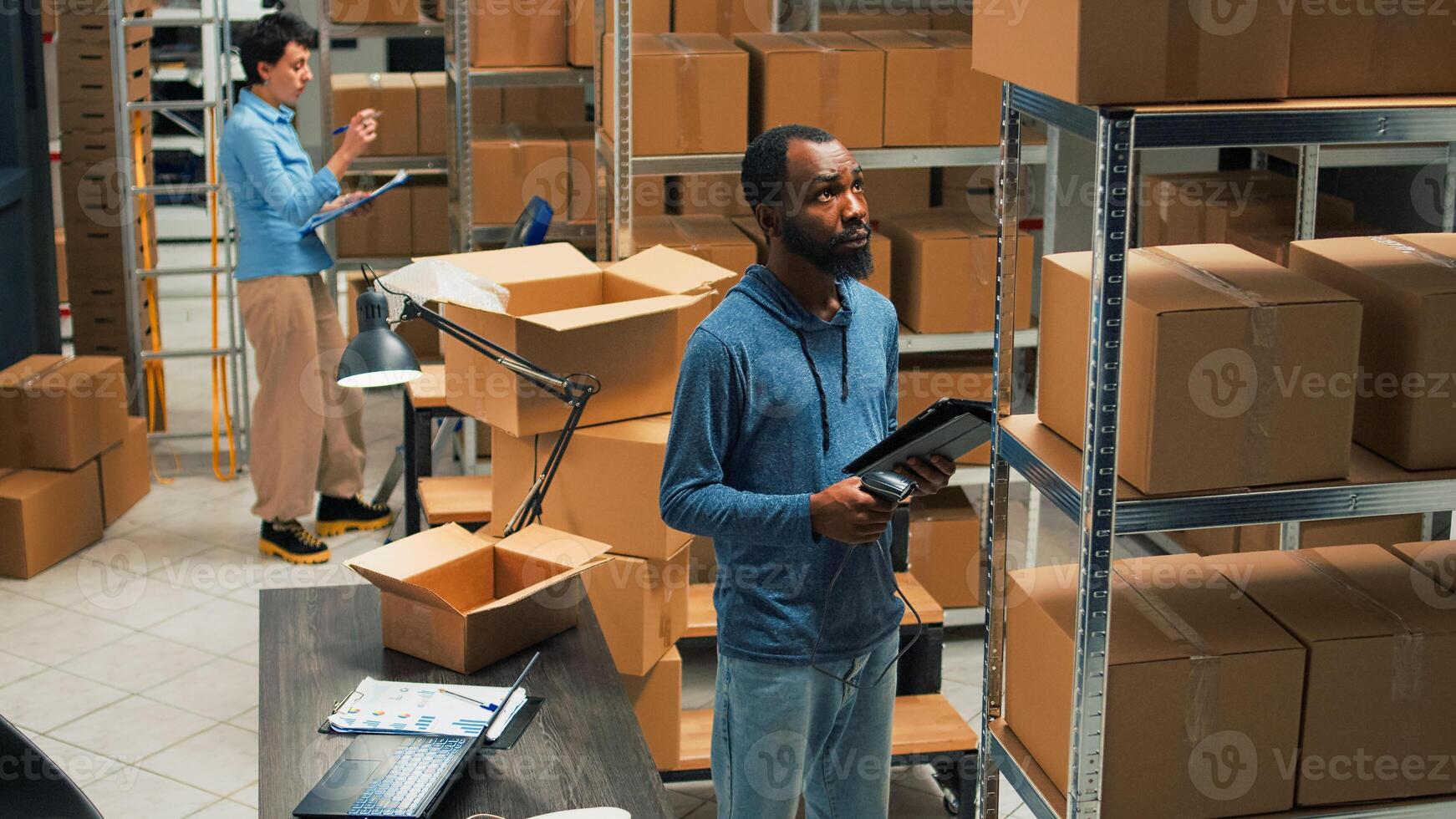 Small business owner scanning bar code on carton boxes, working on doing merchandise inventory in warehouse space. Male worker taking packages from sorage room racks and checking them. photo
