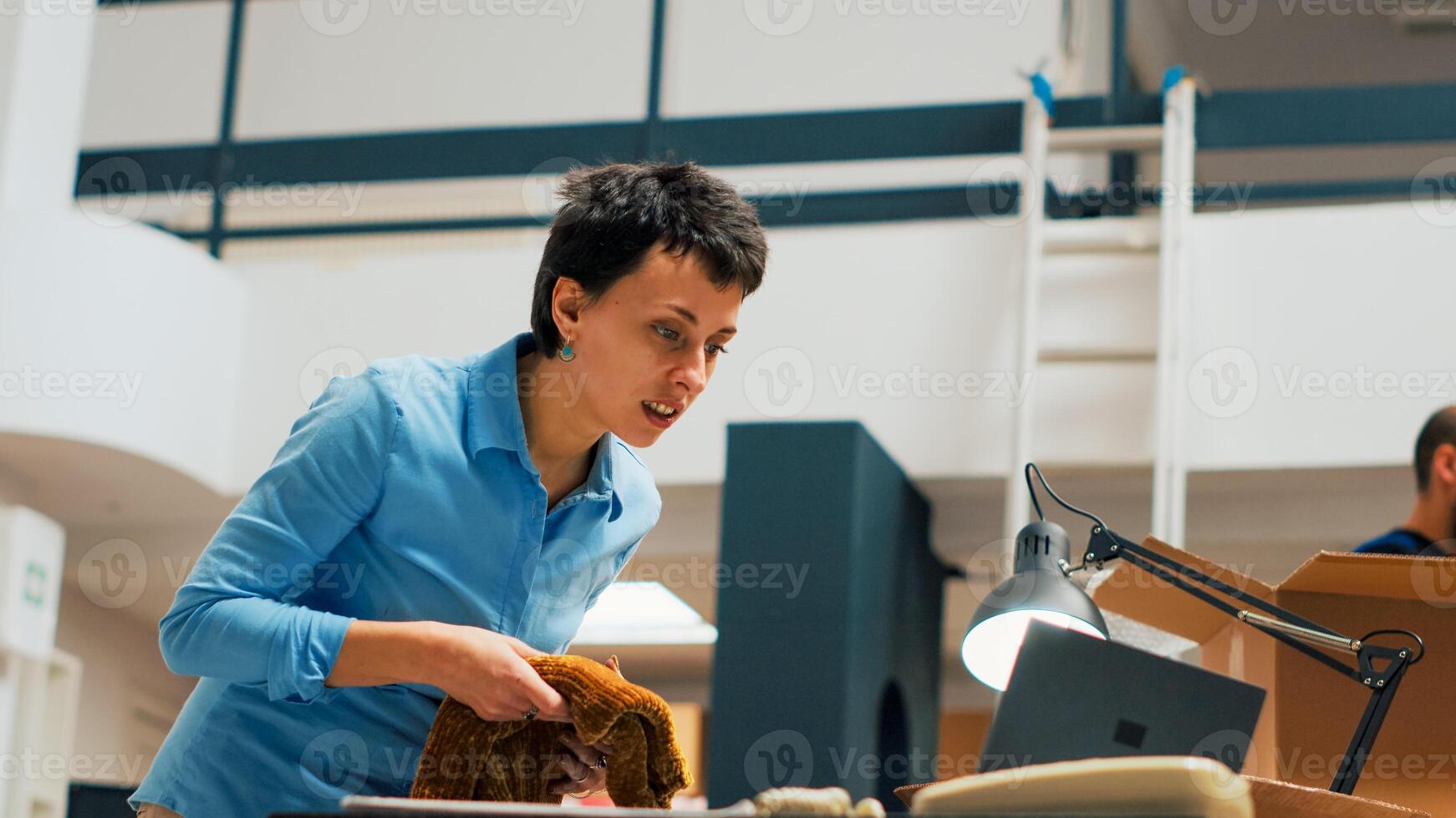 joven negocio propietario poniendo mercancías en cajas a ayuda con envío, trabajando en distribución y gestión. hembra empleado tomando productos desde almacén estantes. Mano disparo. foto