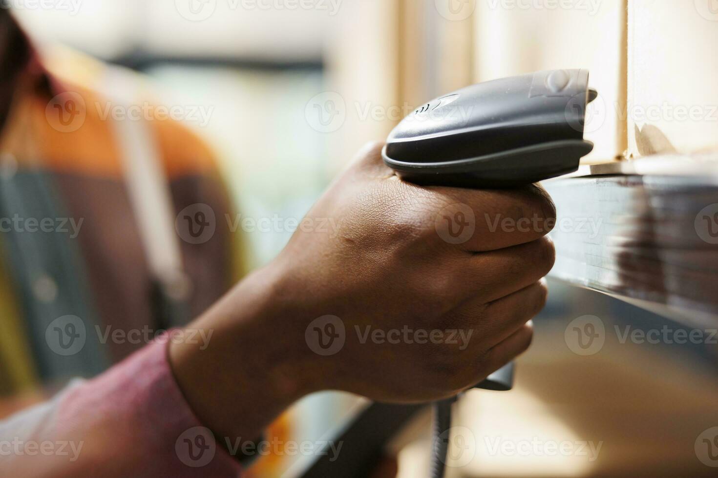African american man hand holding barcode scanner in industrial warehouse. Freight storehouse worker arm scanning cargo cardboard box code for inventory management close up photo