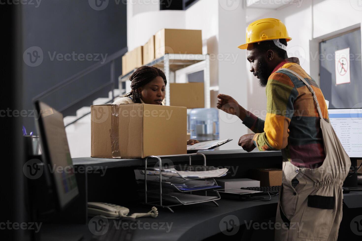 Courier with clipboard bringing parcel to delivery service and register at postal warehouse reception. African american shipment managers checking package documentation at checkout photo