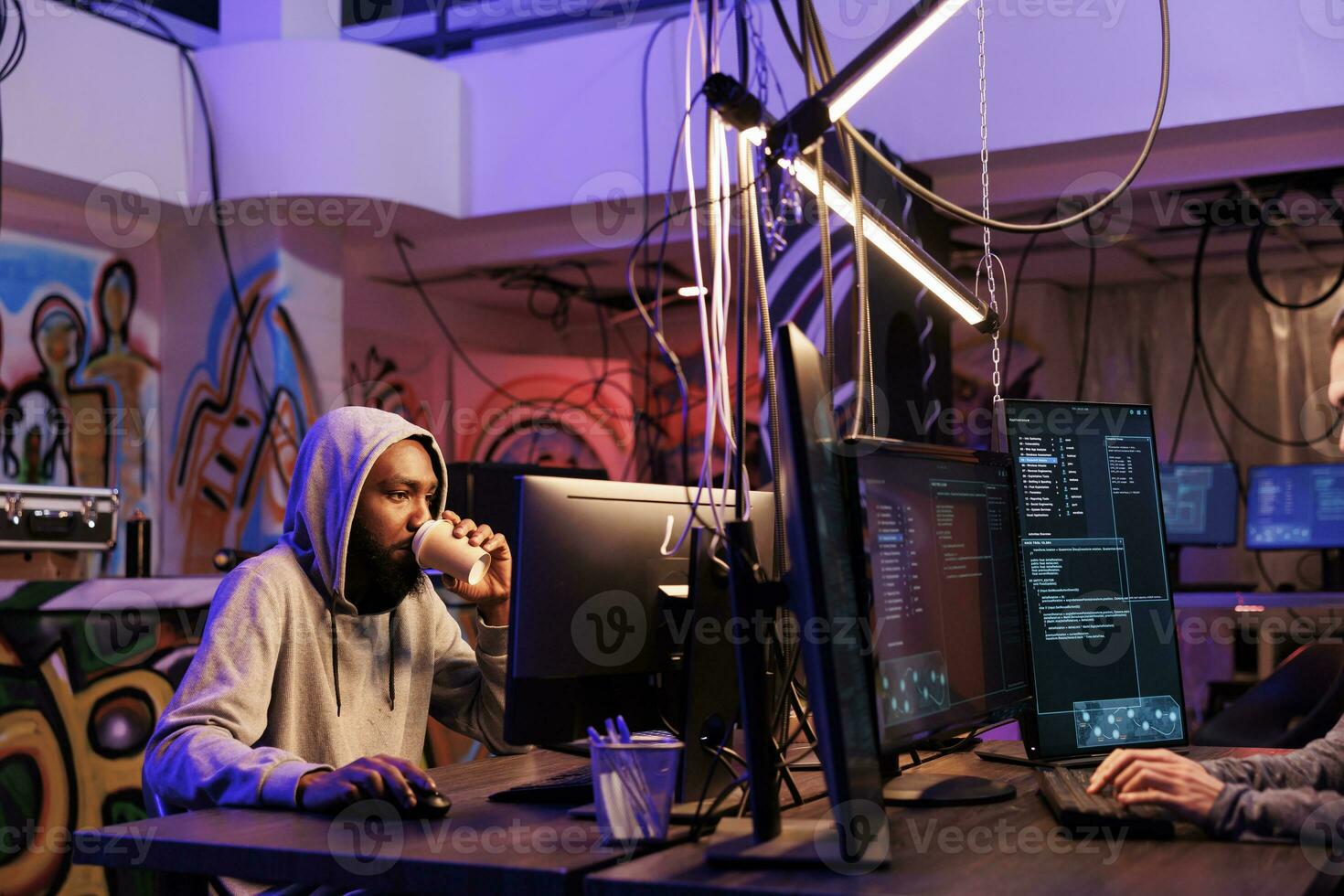 African american hacker drinking coffee and doing illegal activities late. Criminal holding takeaway cup while hacking server and coding malware in abandoned warehouse at night photo