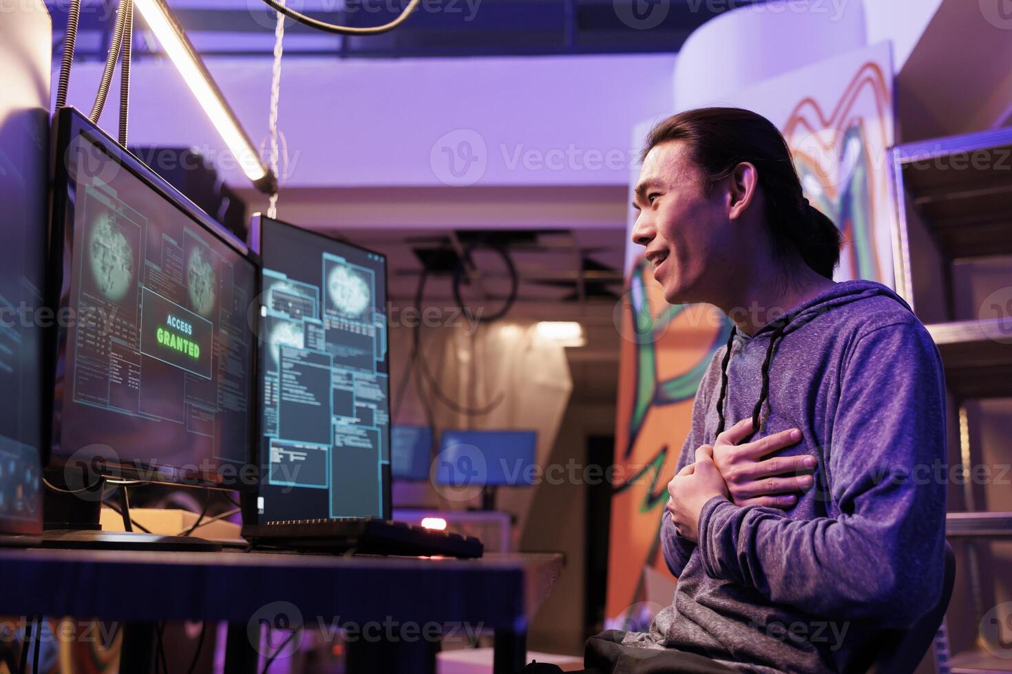 Excited hacking system successfully while doing illegal activities in abandoned warehouse. Happy shocked young asian criminal getting access granted message on computer screen photo