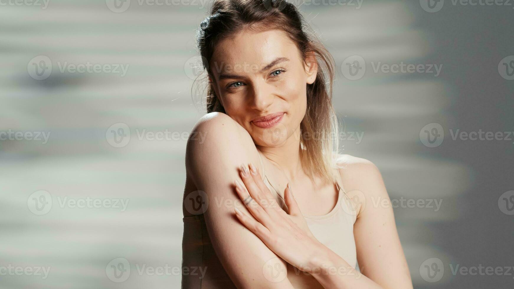 Caucasian lady promoting body cream in studio, filming beauty ad campaign and applying moisturizer and neck and shoulders. Beautiful model using glowing serum and advertising product. photo