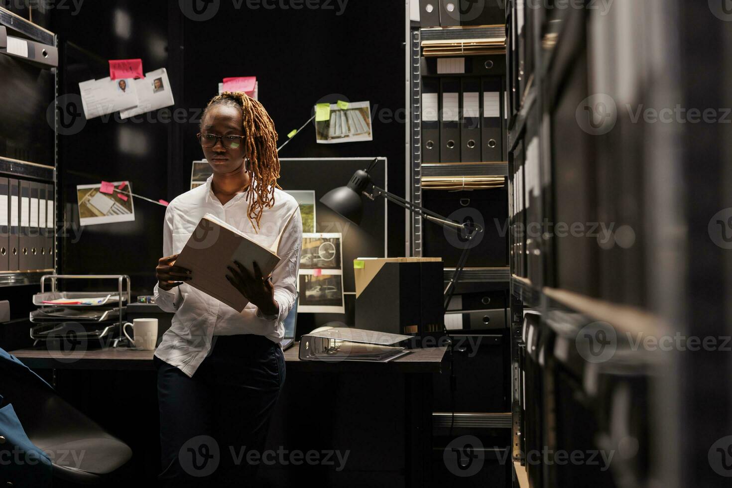 African american woman detective working in investigator office late. Pensive policewoman holding csi conclusion file, thinking about crime solving solution at night time photo