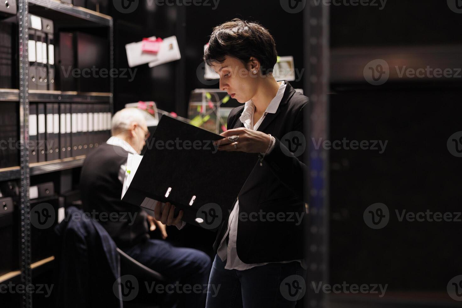 Fbi woman agent holding confidential crime files, working overtime at victim report in arhive room. Criminology workers analyzing suspect information, discussing criminal investigations strategy photo