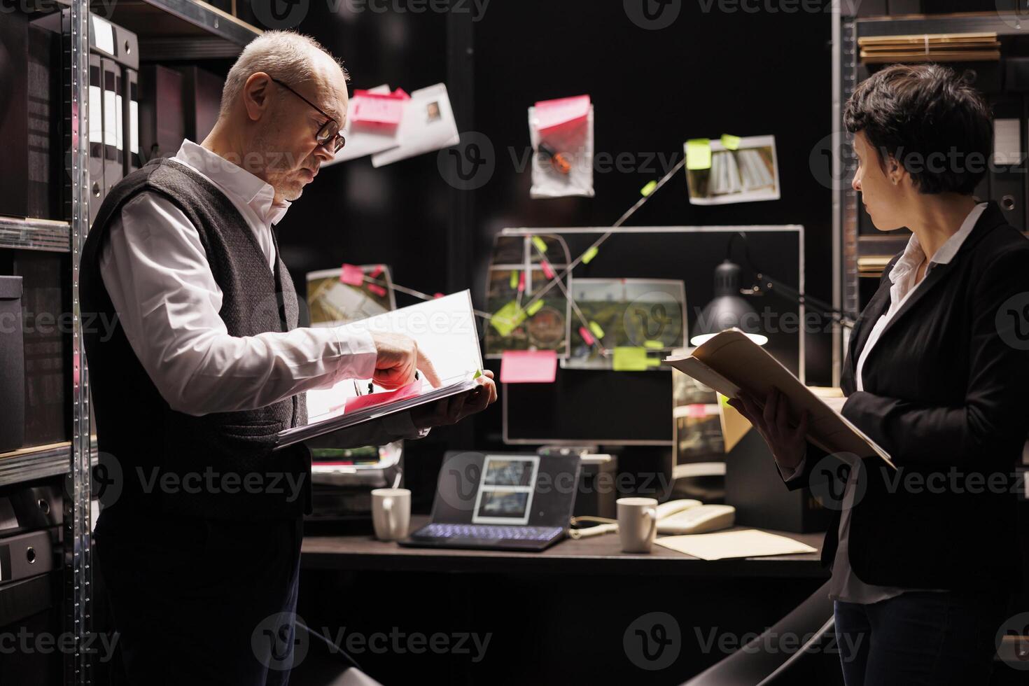 Federal agents working overhours at criminal case, analyzing criminology report in arhive room. Elderly police officer reading suspect declaration while private detective checking victim report photo